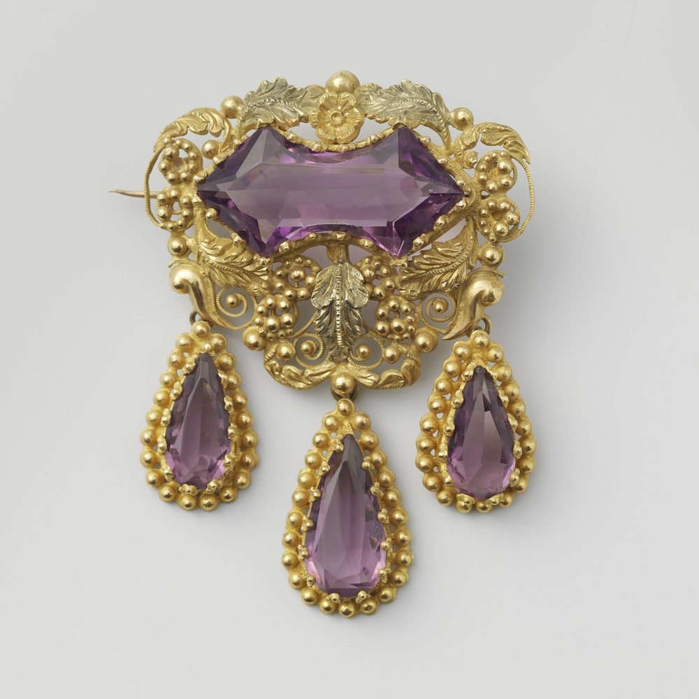 A brooch lying face up, the pin folded flat beneath it.
